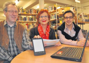 Neue Technik in der Bibliothek: Uwe Schrader (links), EDV-Mitarbeiter im Rathaus, zeigt einen E-Book-Reader. Auf dem kann man künftig ebenso Bücher und Zeitschriften lesen wie auf einem Laptop, wie er vor Regina Howorek und Lars Matiszik auf dem Tisch steht. Foto: J. Wohlgemuth