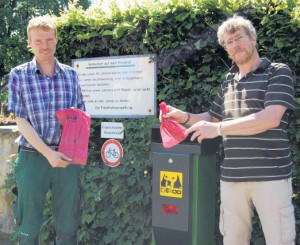 Bitte benutzen: Gut sichtbar hat Friedhofsgärtner Carsten Solfrian (links) die Hundetoiletten aufgestellt und die Verbotsschilder angebracht, Baukirchmeister Rainer Wolf weist auf das Benutzen und Verschließen der Beutel hin. Foto. A. Hein